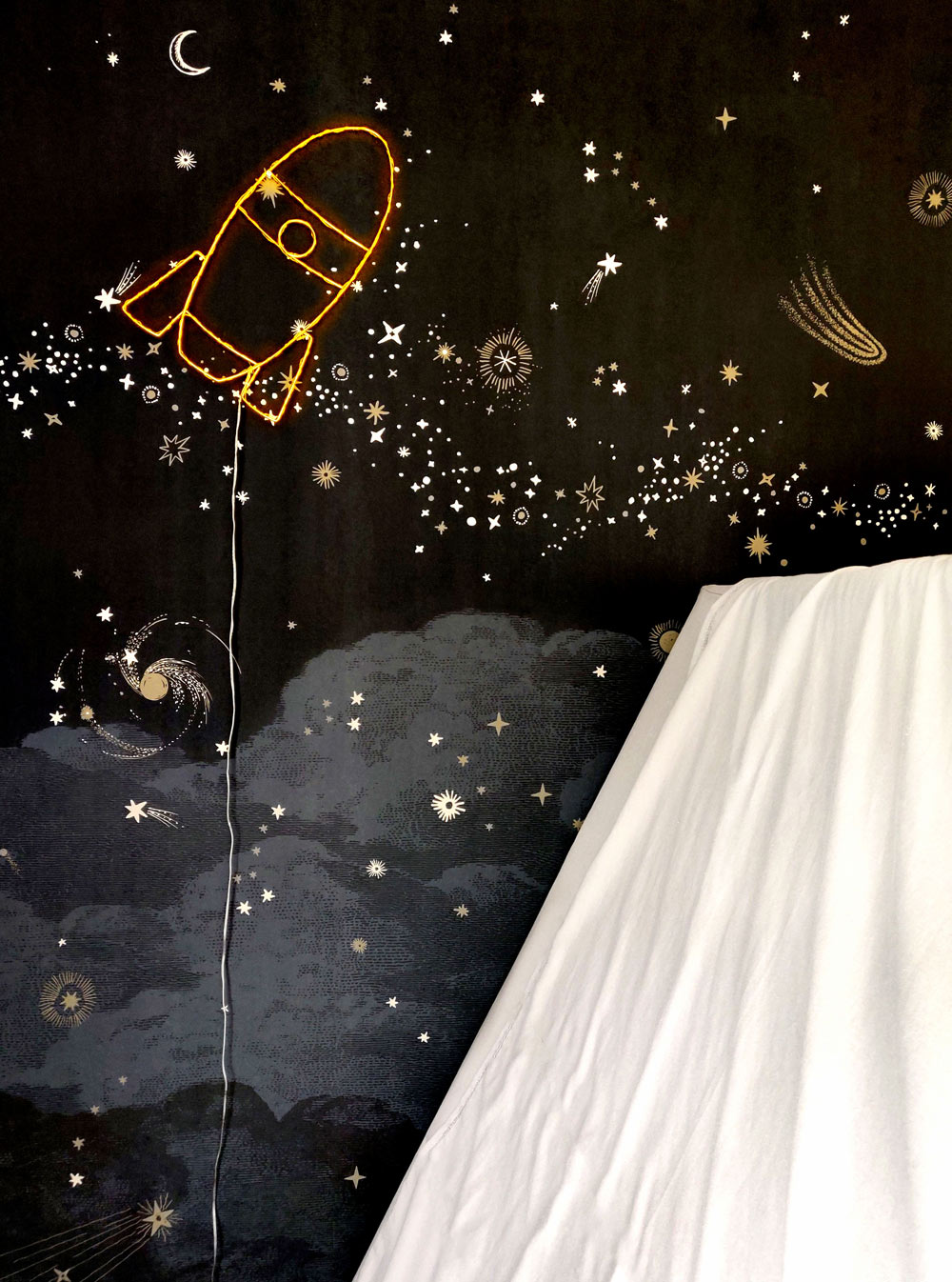 Mur sur lequel se trouve un néon en forme de fusée jaune avec des étoiles